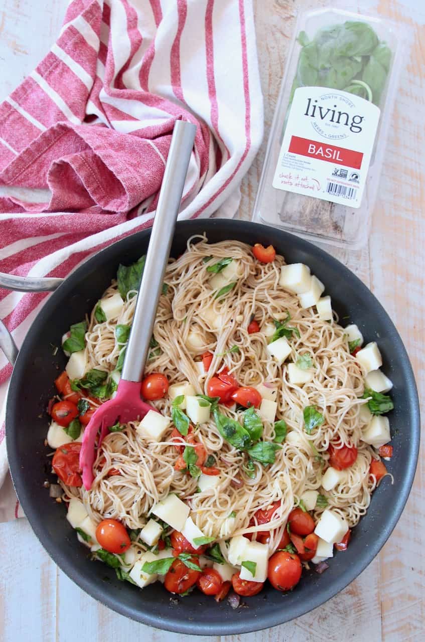 caprese pasta in skillet with red serving spoon with fresh basil on the side