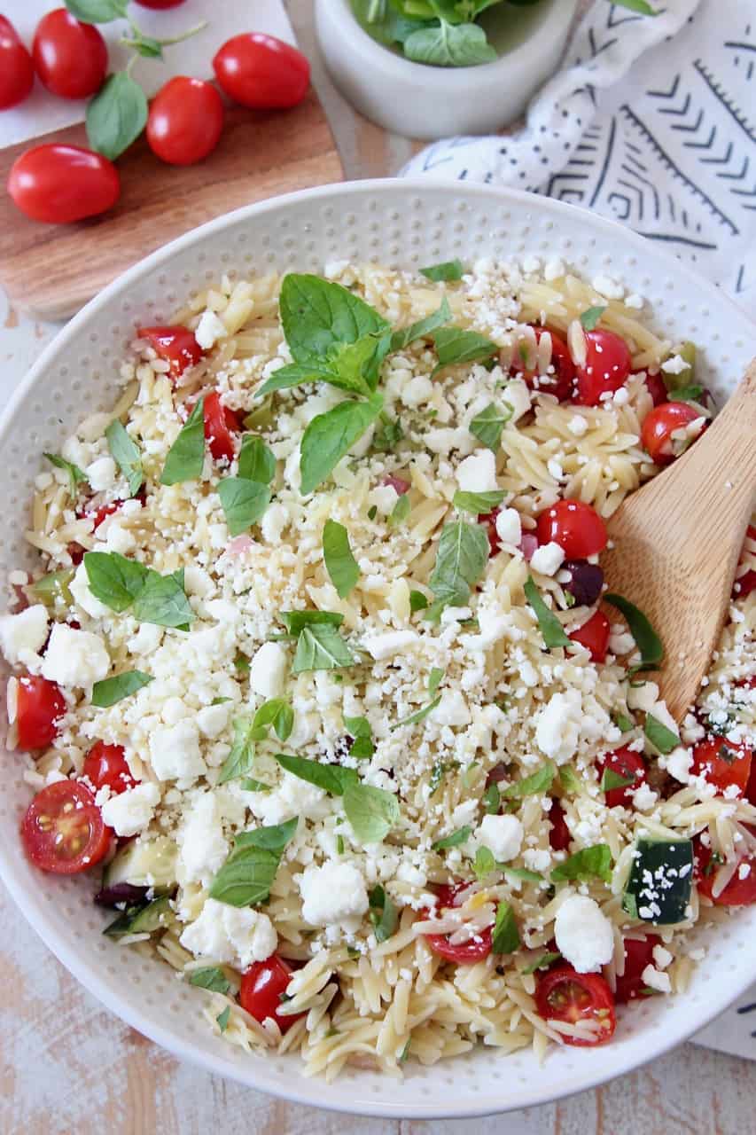 greek orzo salad in bowl with wooden spoon