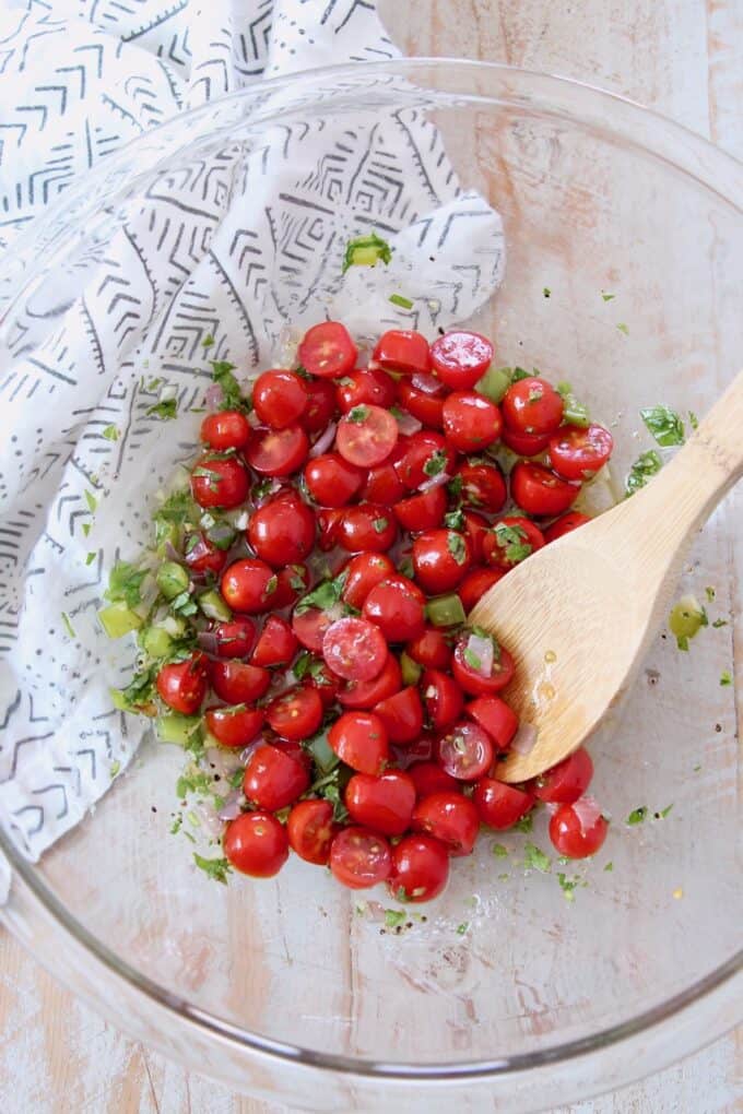 grape tomatoes with lemon herb dressing in glass bowl with wooden spoon