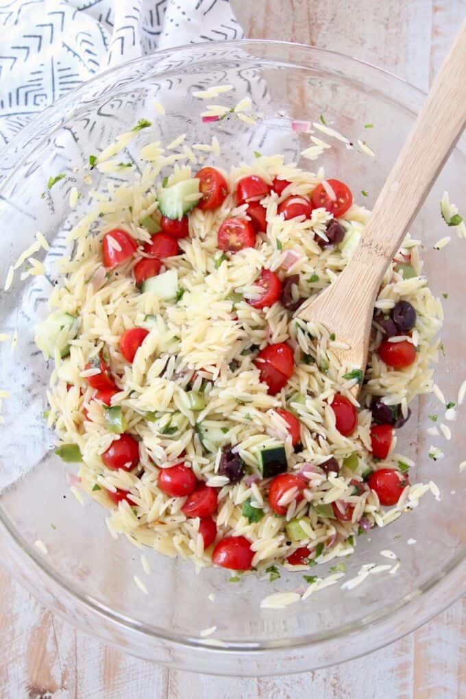 orzo salad in glass bowl with wooden spoon