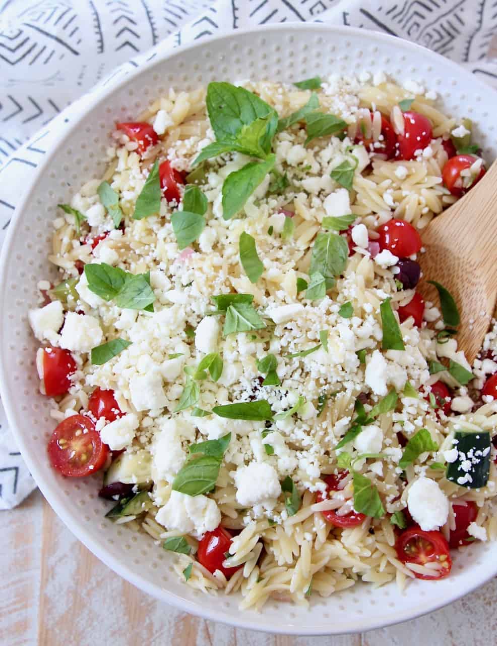 orzo salad with tomatoes and feta in bowl with wooden spoon
