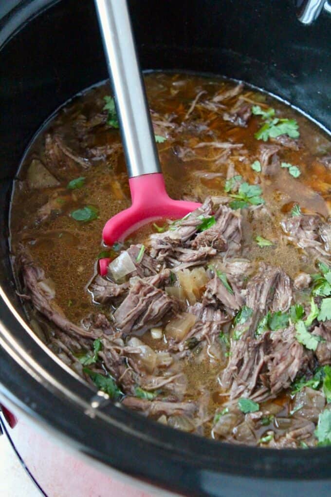 shredded beef in crock pot with red serving spoon
