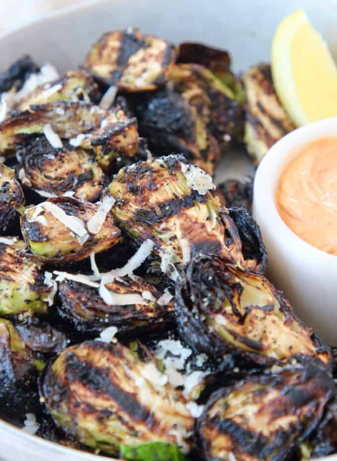 grilled brussels sprouts in bowl with lemon wedge and harissa tahini sauce