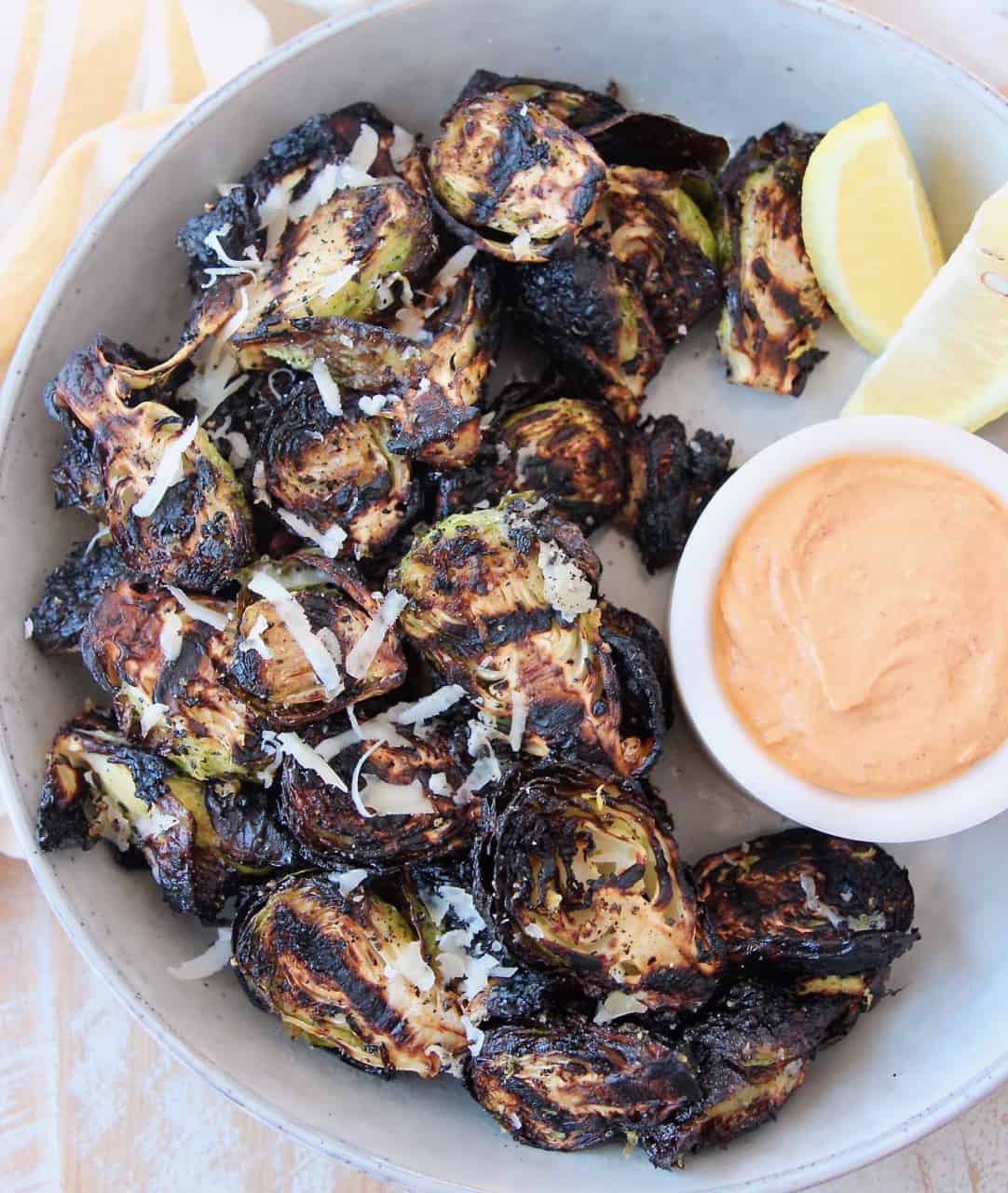 grilled brussels sprouts in bowl with harissa tahini dipping sauce on the side