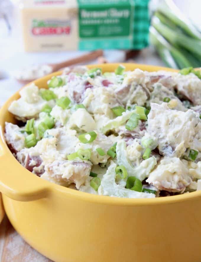 potato salad with celery and green onions in yellow bowl