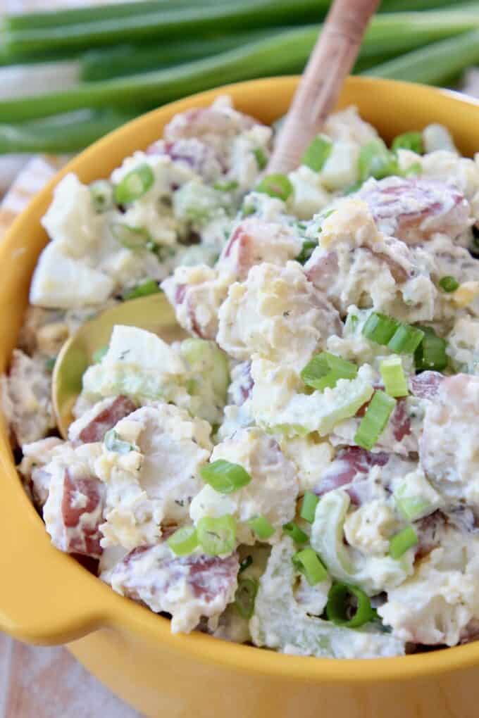 potato salad in yellow bowl with serving spoon