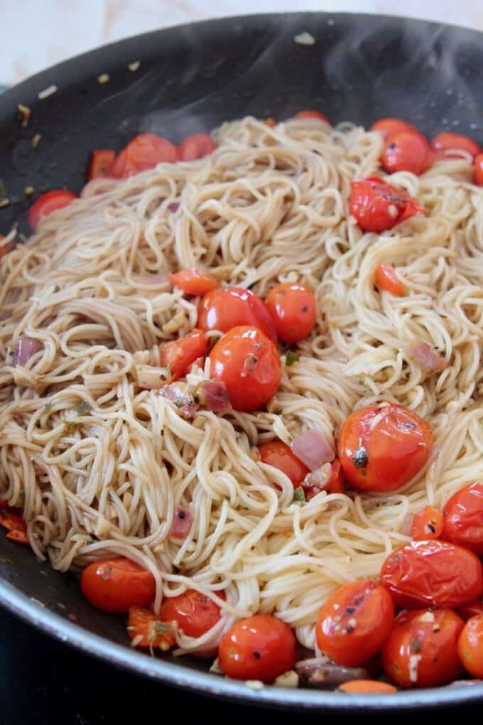 cooked angel hair pasta in a skillet tossed with seasoned cherry tomatoes