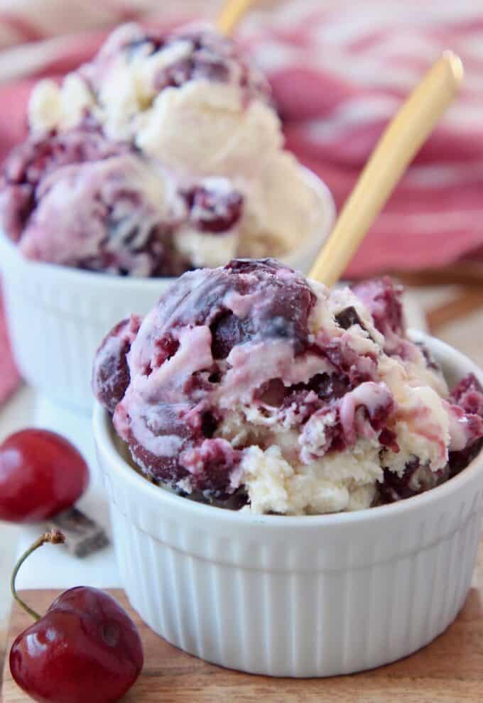 scoops of cherry chocolate chunk ice cream in white bowls with gold spoons