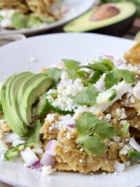 chilaquiles verdes on white plate topped with fresh cilantro and sliced avocado