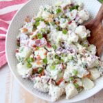 potato salad in white bowl with wooden serving spoon