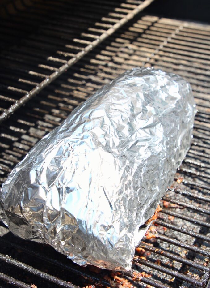 pork shoulder wrapped in foil on a smoker