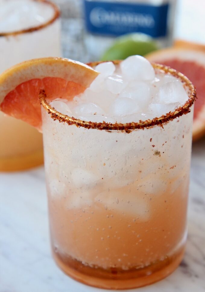 paloma in glass with ice and tajin rim on the glass with a grapefruit wedge