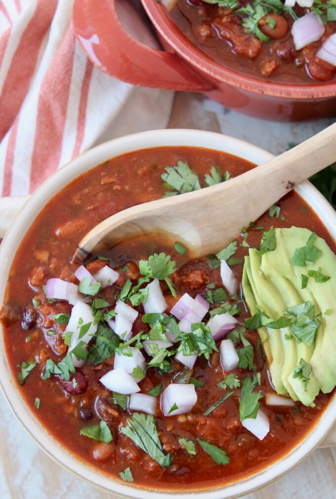 vegan chili in bowl with spoon and sliced avocado