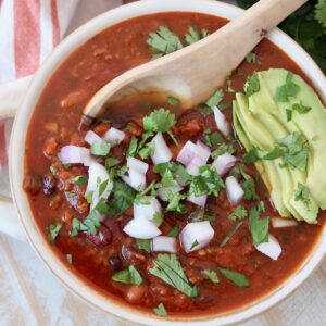chili in bowl topped with diced onions and sliced avocado