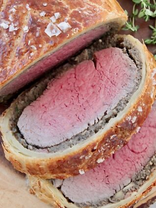 sliced cooked beef wellington on wood board with fresh thyme