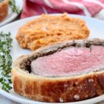 slice of beef wellington on place with mashed sweet potatoes and fresh herbs