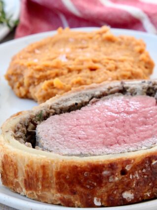 slice of beef wellington on place with mashed sweet potatoes and fresh herbs