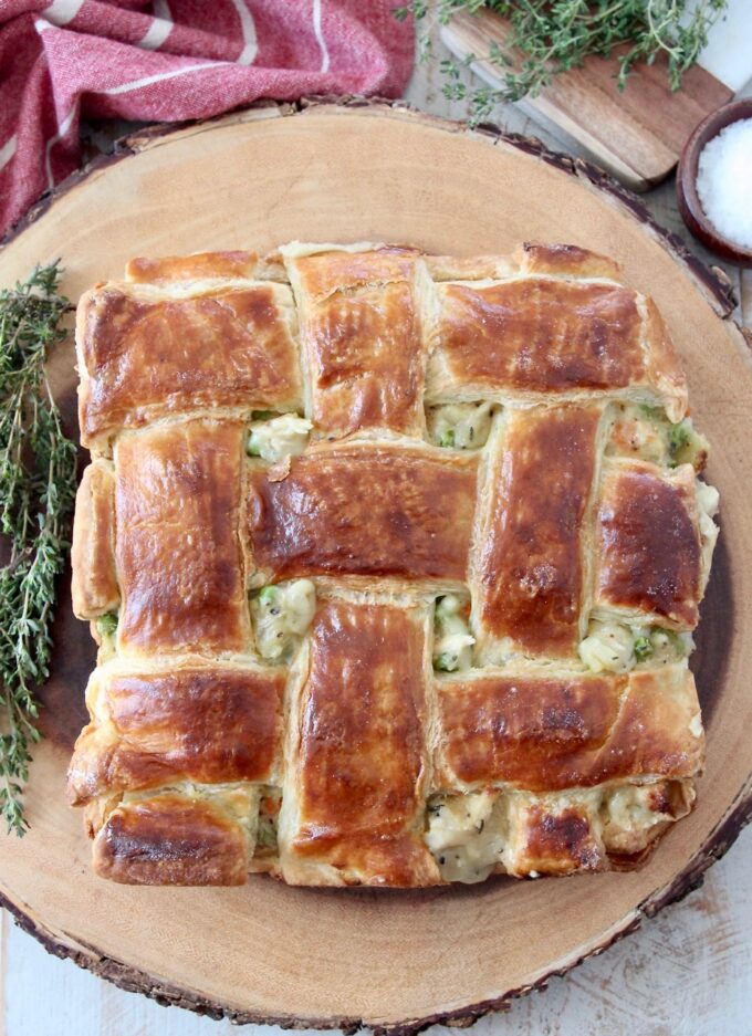 baked chicken pot pie with puff pastry crust on wood serving tray with fresh thyme
