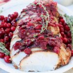 sliced turkey breast covered with cranberry sauce and fresh thyme sprigs on white plate