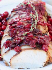sliced turkey breast covered with cranberry sauce and fresh thyme sprigs on white plate