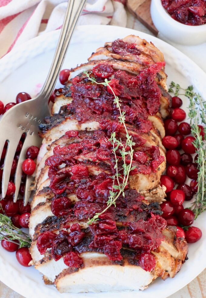 sliced turkey breast covered in cranberry sauce on plate with large serving fork