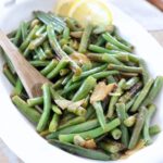 cooked green beans in white serving bowl with spoon