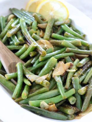 cooked green beans in white serving bowl with spoon