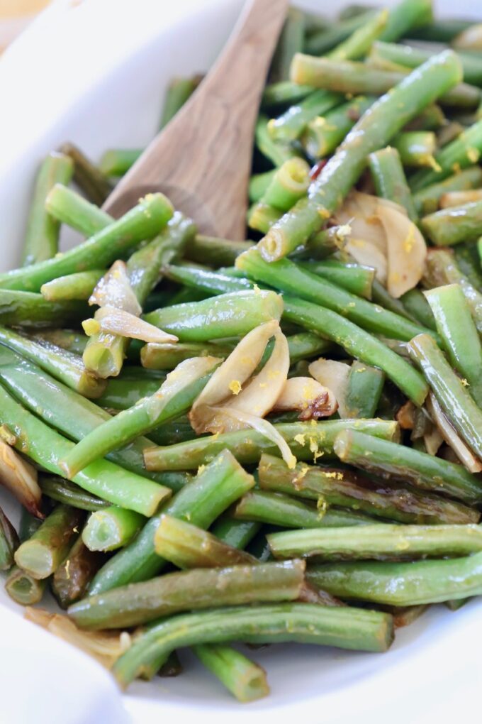 cooked green beans in white serving bowl with wooden spoon