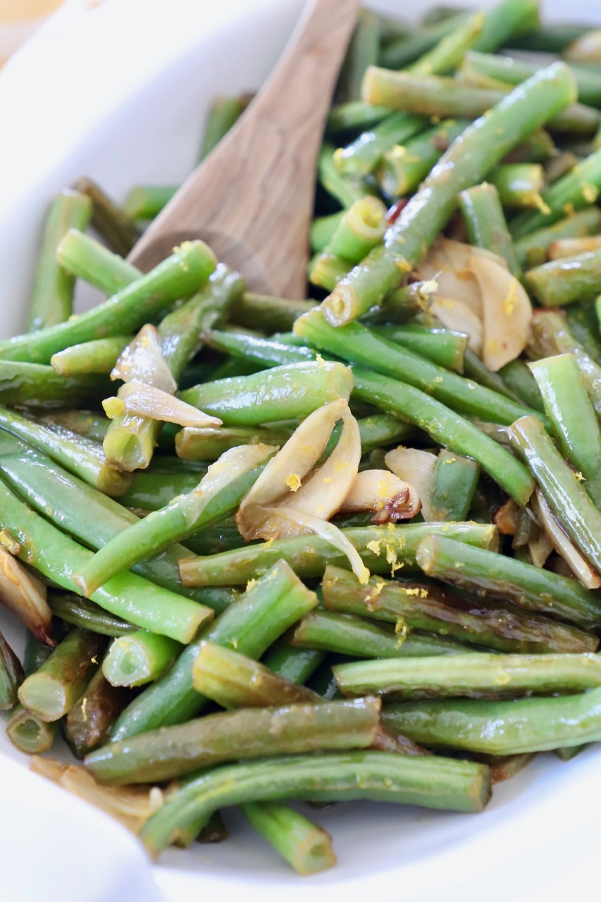 cooked green beans in white serving bowl with wooden spoon