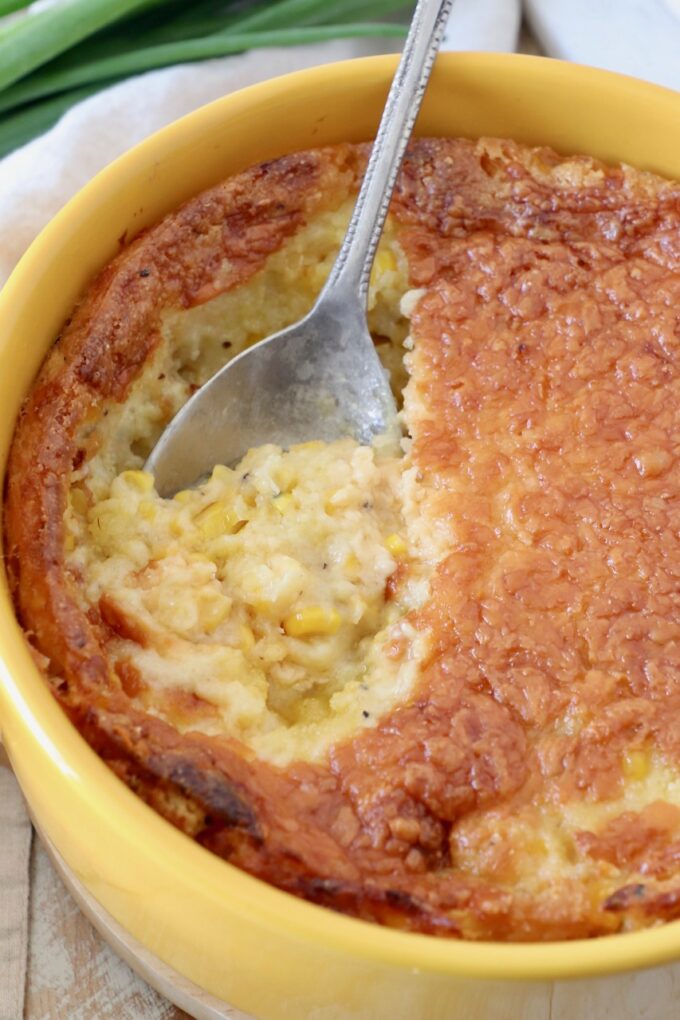 corn casserole in yellow round baking dish with serving spoon