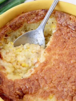 corn casserole in yellow baking dish with silver serving spoon