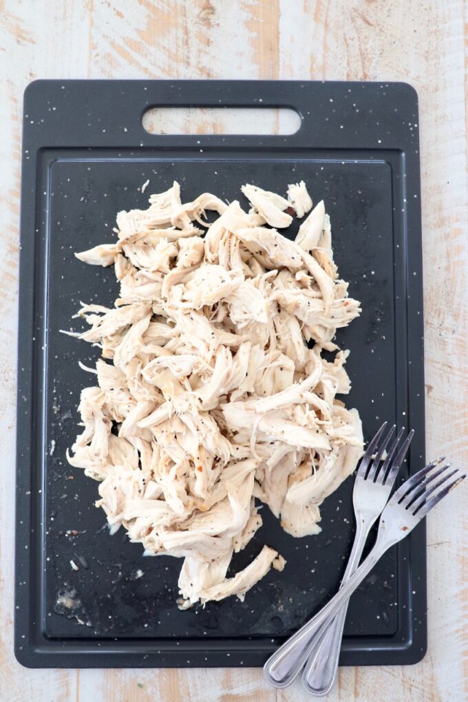 shredded chicken on a cutting board with two forks on the side