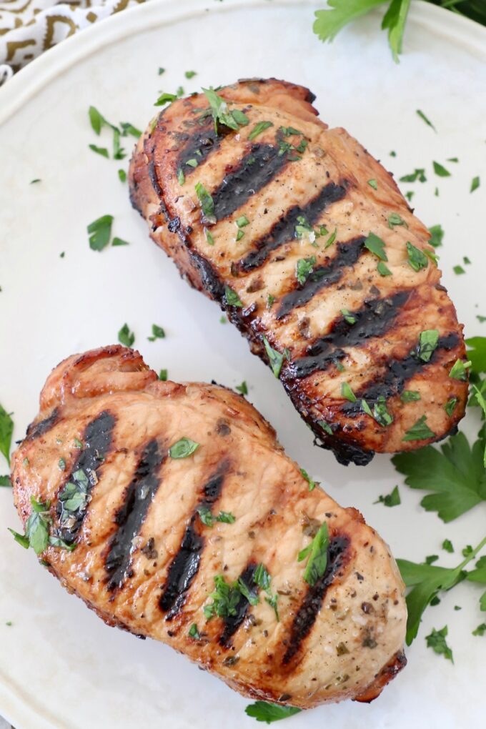two grilled pork chops on plate topped with fresh chopped herbs