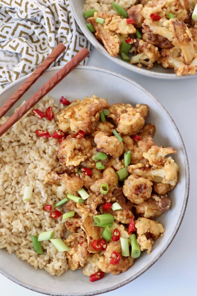 fried cauliflower in bowl with brown rice and chopsticks