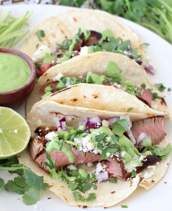 steak tacos on plate with cilantro sauce and fresh lime