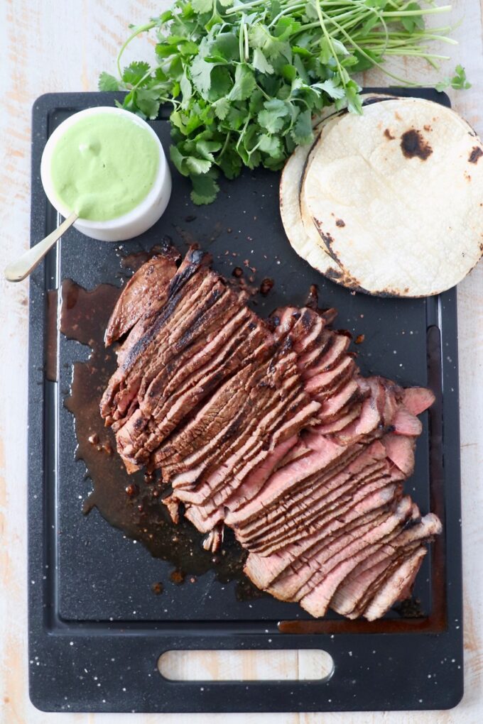 sliced steak on cutting board with sauce and tortillas