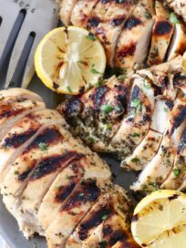 sliced grilled chicken on plate with lemons