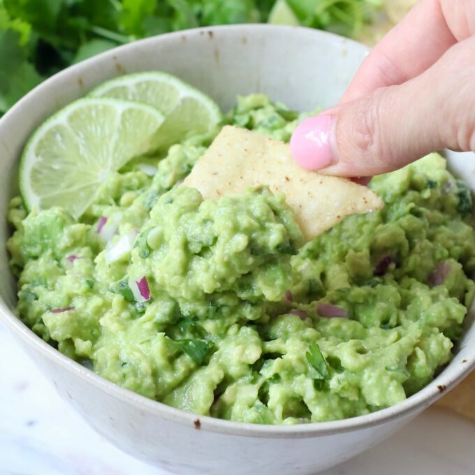 hand dipping tortilla chip into bowl of guacamole