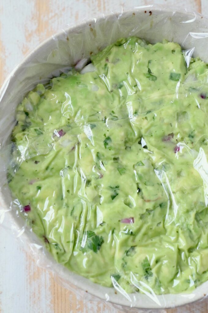 guacamole in bowl with plastic wrapped pressed on top