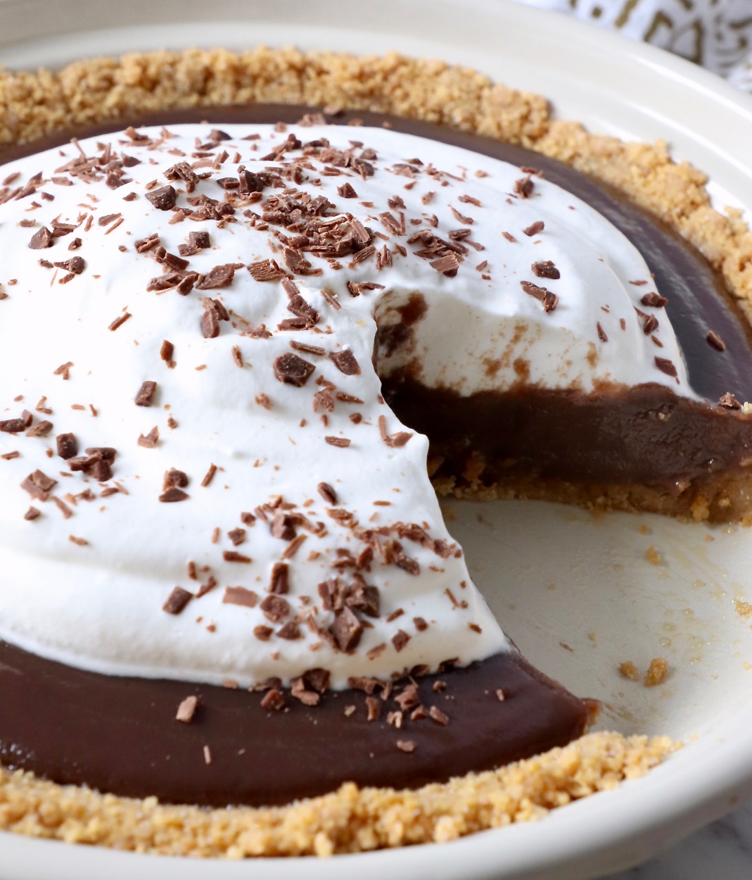chocolate pie with whipped cream topping in pie plate with slice taken out of the pie