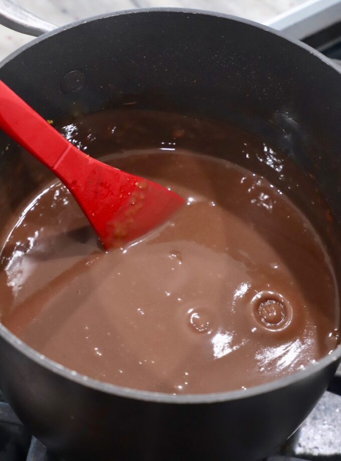red spoon stirring chocolate pie filling in saucepan