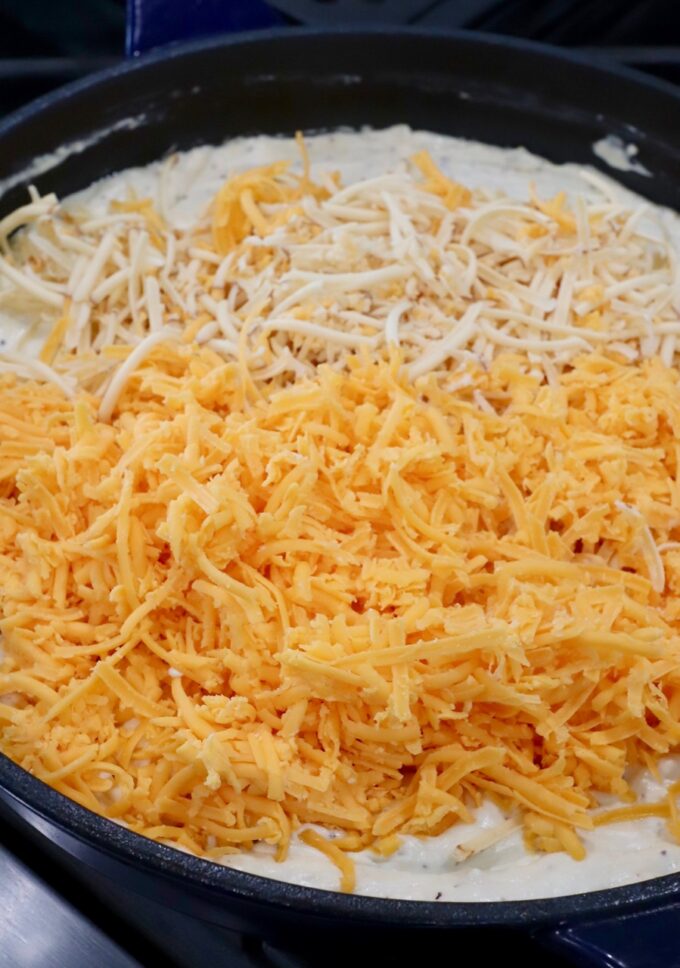 shredded cheese in skillet of creamy sauce