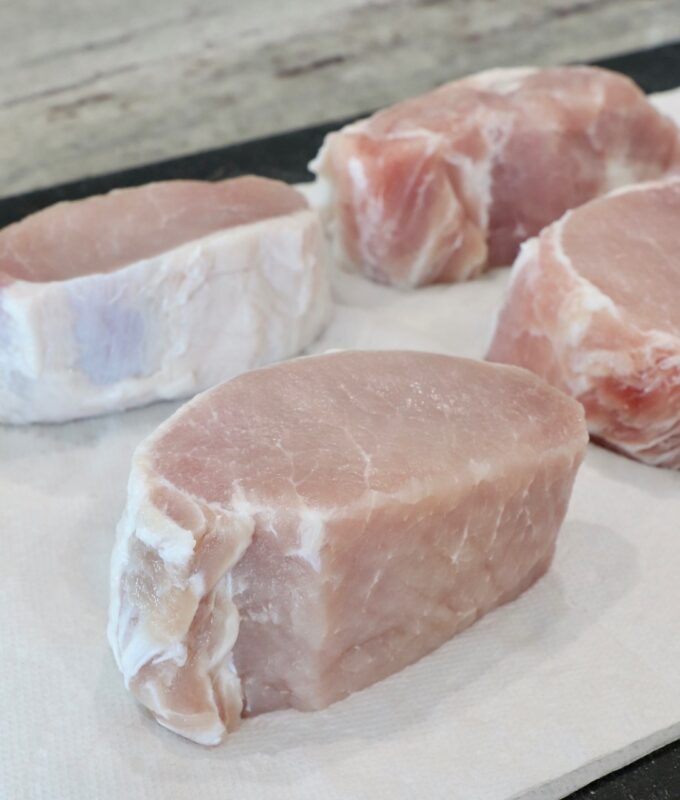 thick pork chops sitting on paper towels on a cutting board