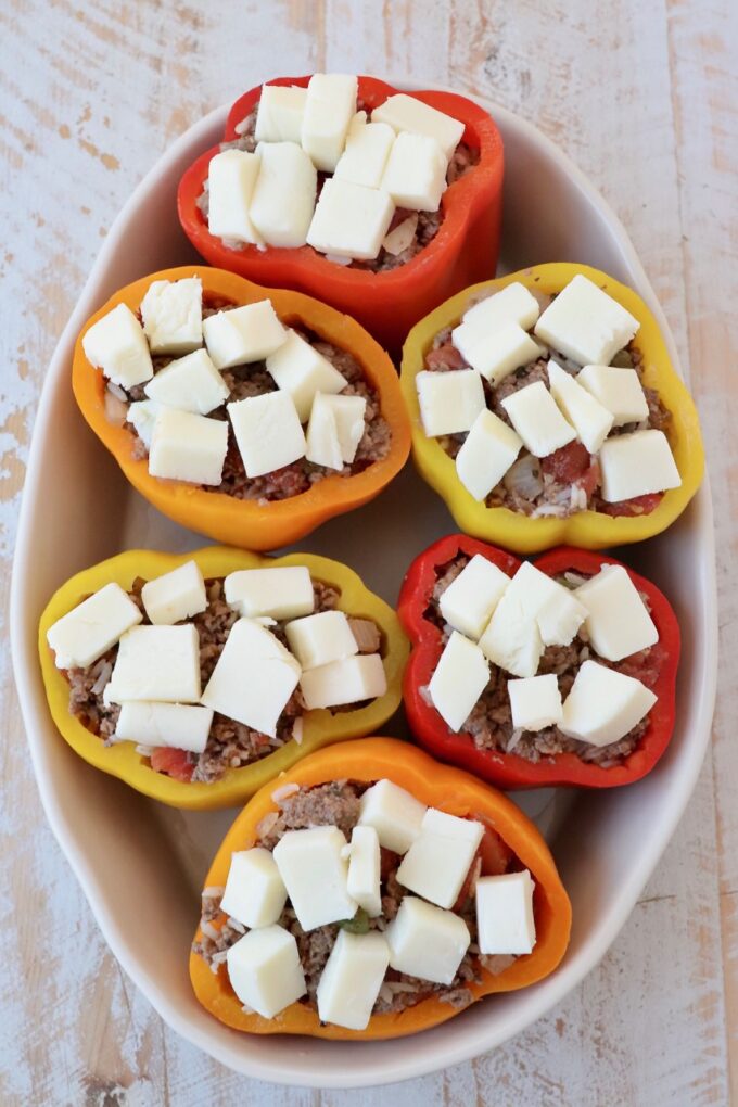 stuffed bell peppers topped with cubes of cheese in oval casserole dish