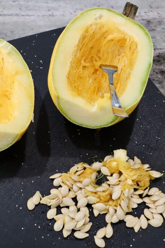 spaghetti squash cut in half on cutting board, with seeds removed on the side of the board