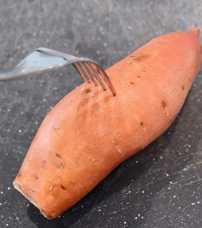 fork piercing sweet potato on cutting board
