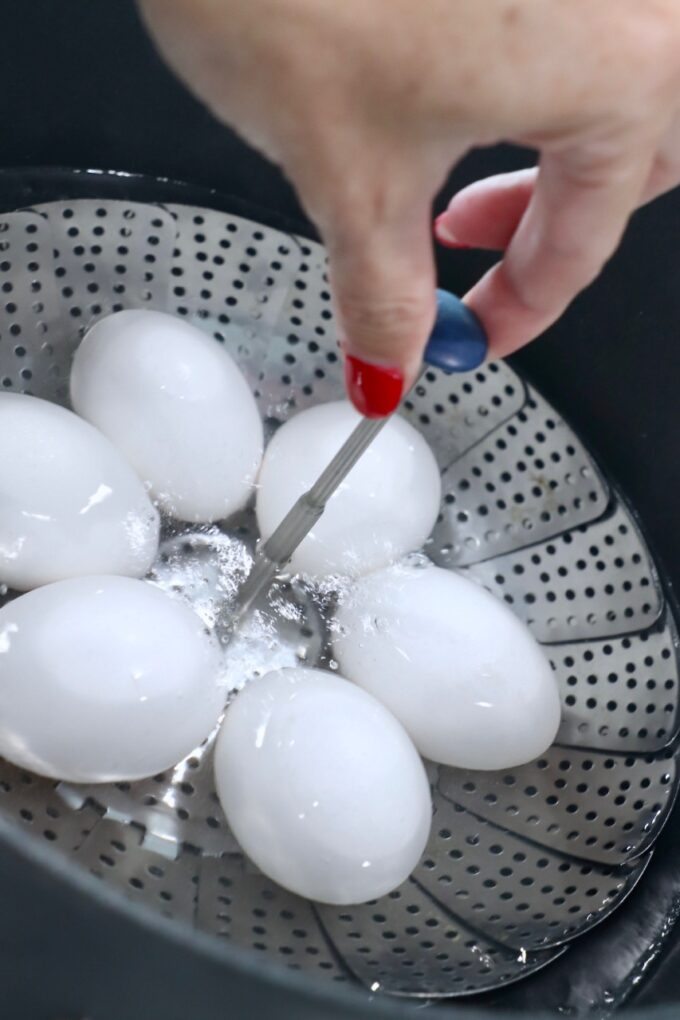 hand lowering eggs in steamer basket into pot of boiling water
