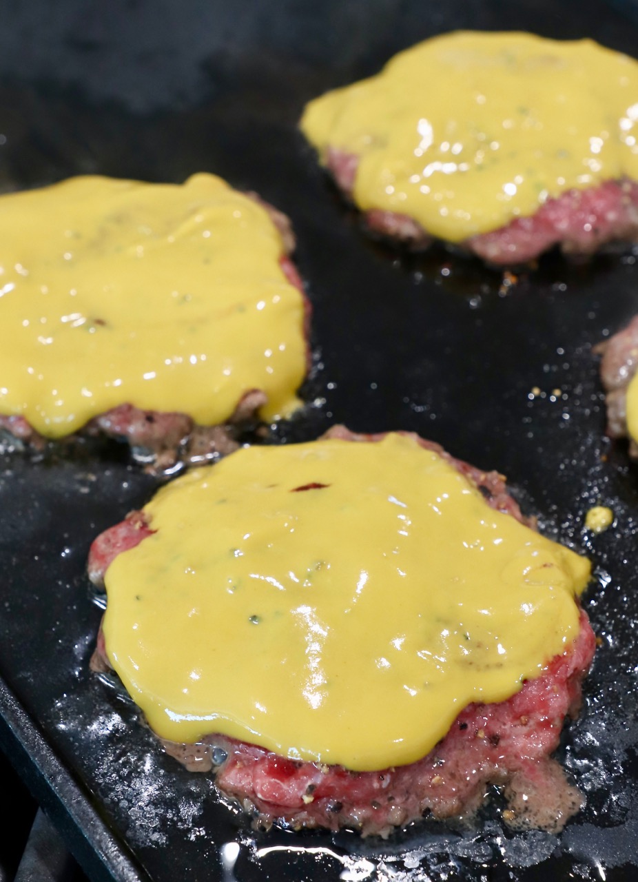 mustard covered burger patties on cast iron griddle