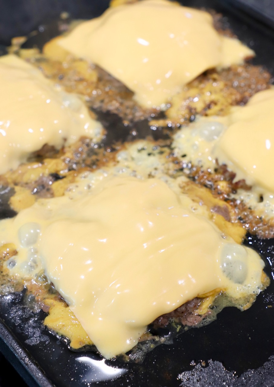 cheese covered burger patties at griddle