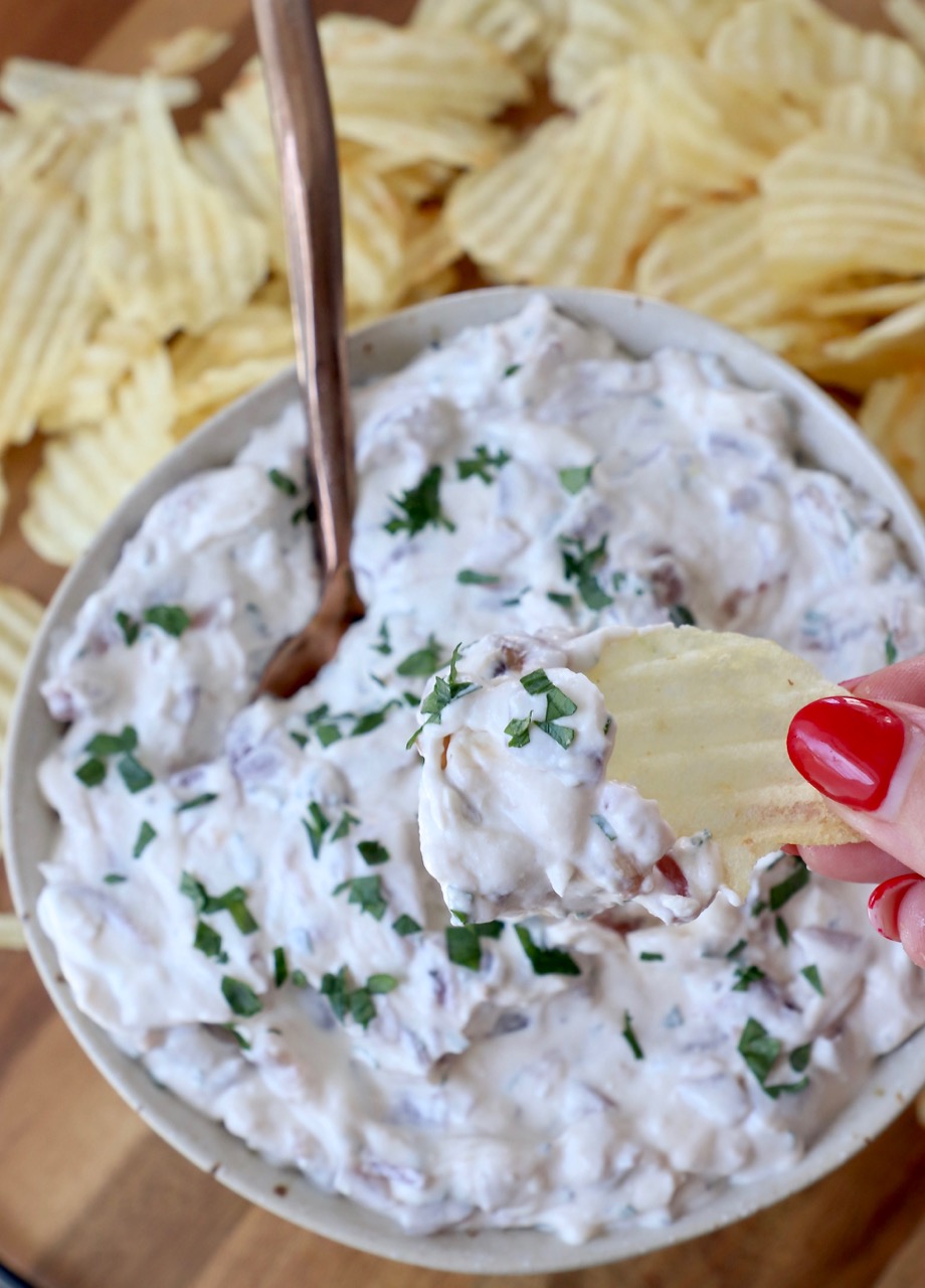 hand dipping chip into french onion dip in bowl